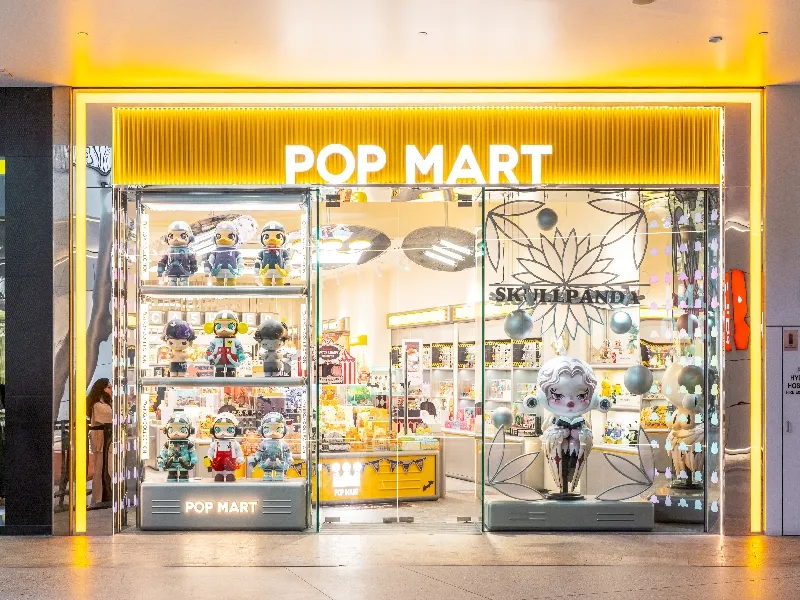 POP MART store with bright yellow signage displaying colorful collectible figures and toys in illuminated glass window cases.